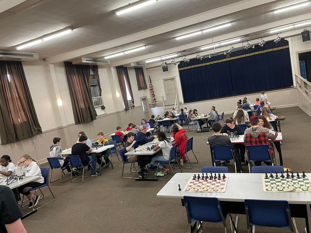 Students seated at tables competing in chess tournament. 