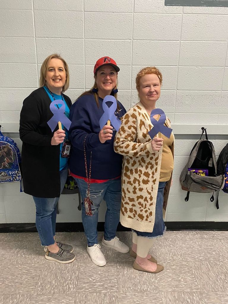 Three teachers holding up blue ribbons.