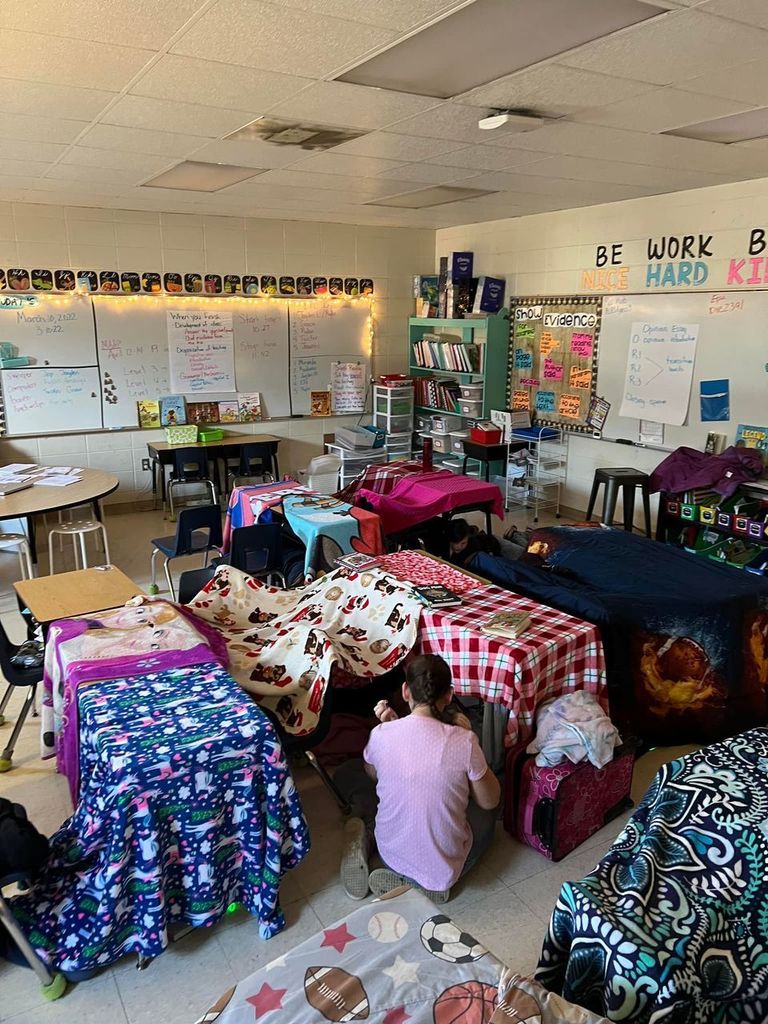 Image of classroom with blankets hanging over desks as students gather under them.
