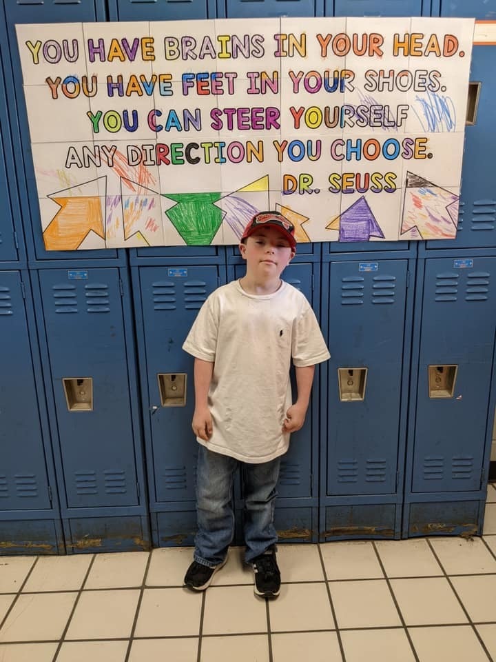 Male student standing in front of blue lockers. A poster with the following Dr. Seuss quote is on the lockers, "You have brains in your head. You have feet in your shoes. You can steer yourself any direction you choose."